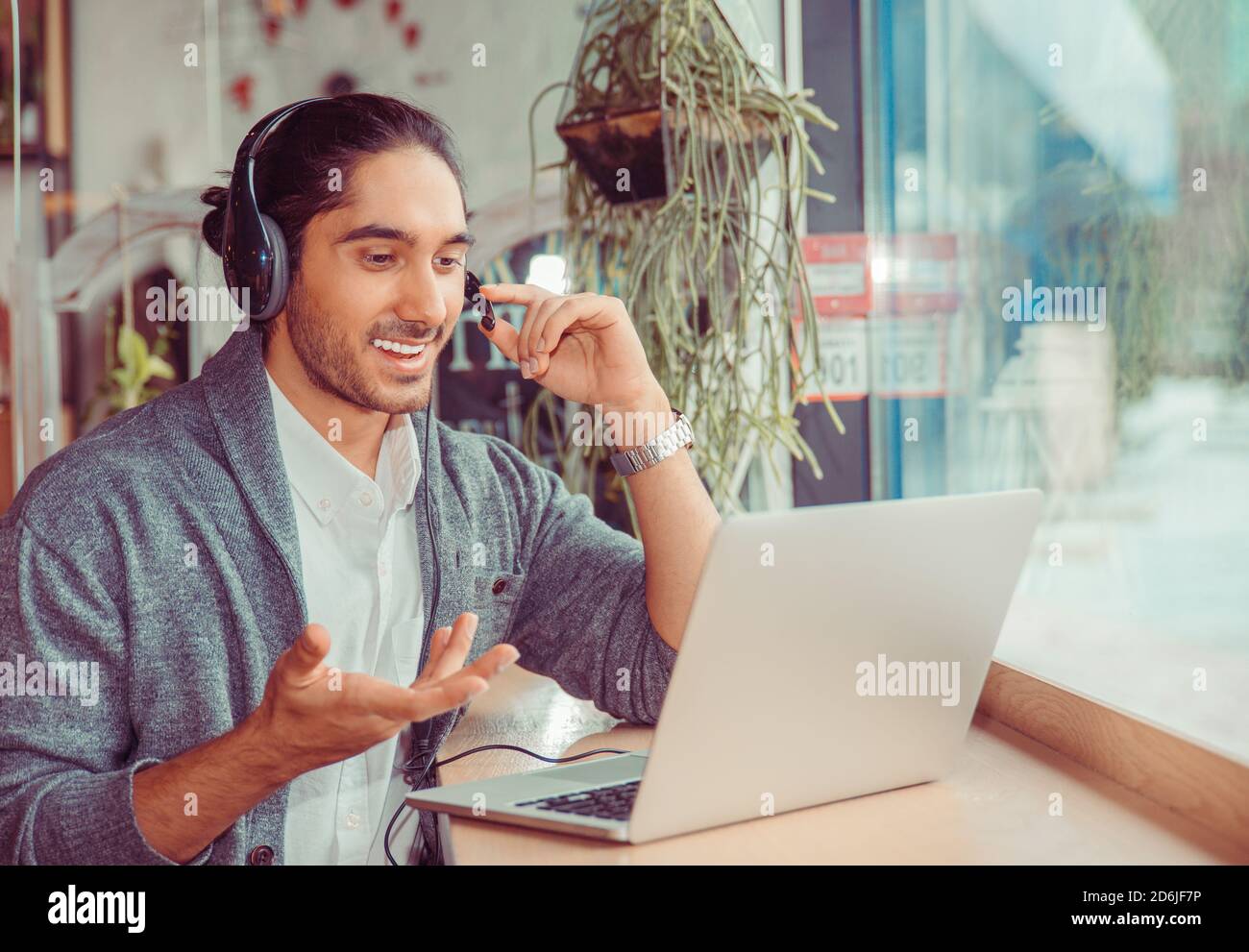 Mann lächelnd mit einem on-line-Gespräch am Laptop Bildschirm suchen, erklärt etwas zu Hause gestikulierend im Wohnzimmer, in der Nähe der Fenster holding Kopf Stockfoto
