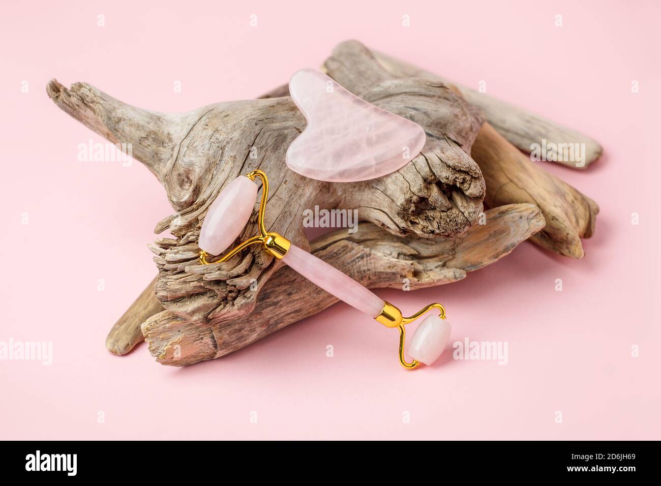 Gua Sha rosa Quarz-Massagegerät und Jadewalze auf rosa Pastell Hintergrund. Jadestein für Gesichts- und Körperpflege. Horizontaler Spross, holzige Pflanzenwurzel, stilvoll Stockfoto