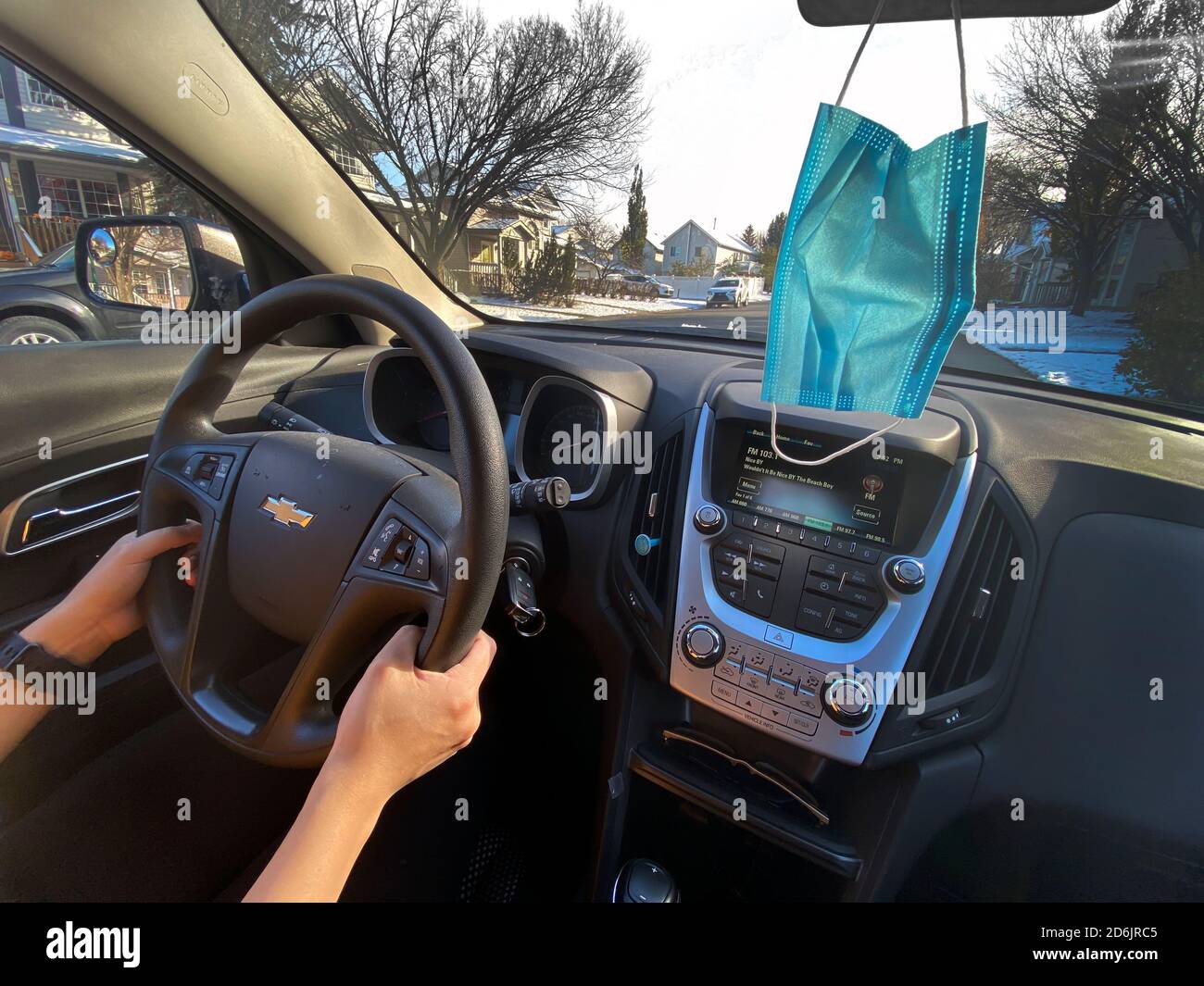 Calgary, Alberta, Kanada. Oktober 17 2020. Eine Person, die an einem sonnigen Tag ein Chevrolet Auto fährt, mit einer Gesichtsmaske, die vom Spiegel hängt. Cocept: Fahren während Stockfoto