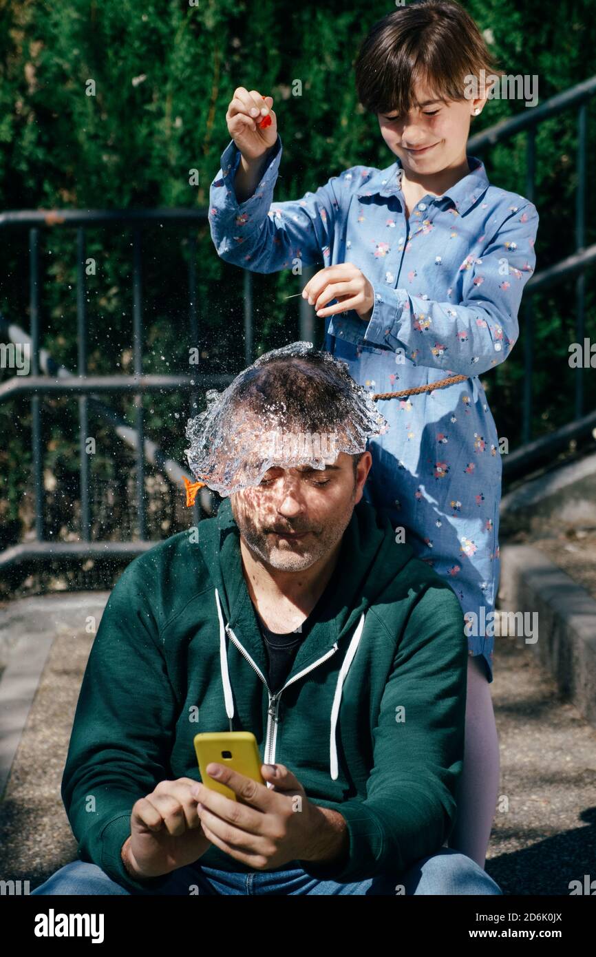 Mädchen sprengte einen mit Wasser gefüllten Ballon über den Kopf ihres Vaters Stockfoto