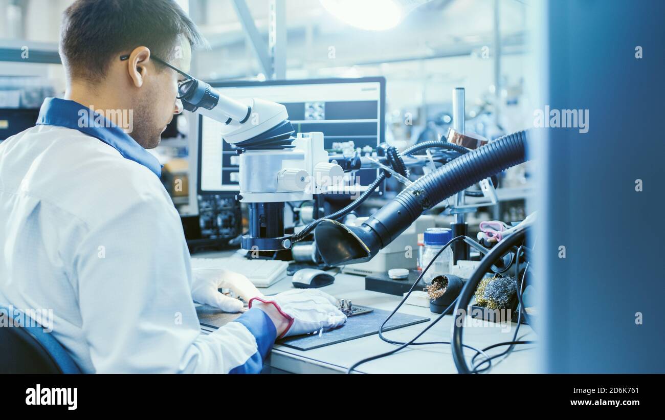 Arbeiter in der Elektronikfabrik in White Work Coat inspiziert eine Leiterplatte über ein digitales Mikroskop. High-Tech-Fabrik. Stockfoto