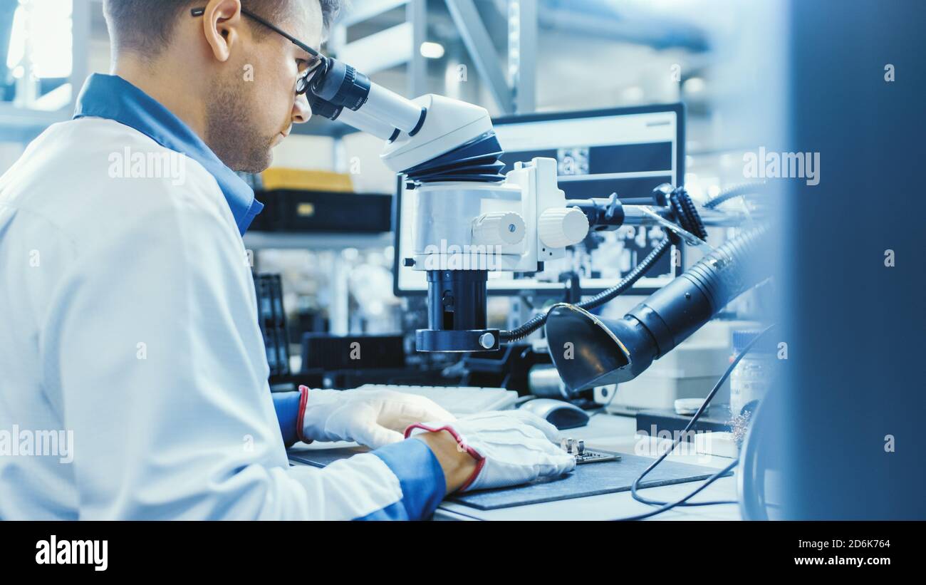 Arbeiter in der Elektronikfabrik in White Work Coat löten eine Leiterplatte über ein digitales Mikroskop. High-Tech-Fabrik. Stockfoto
