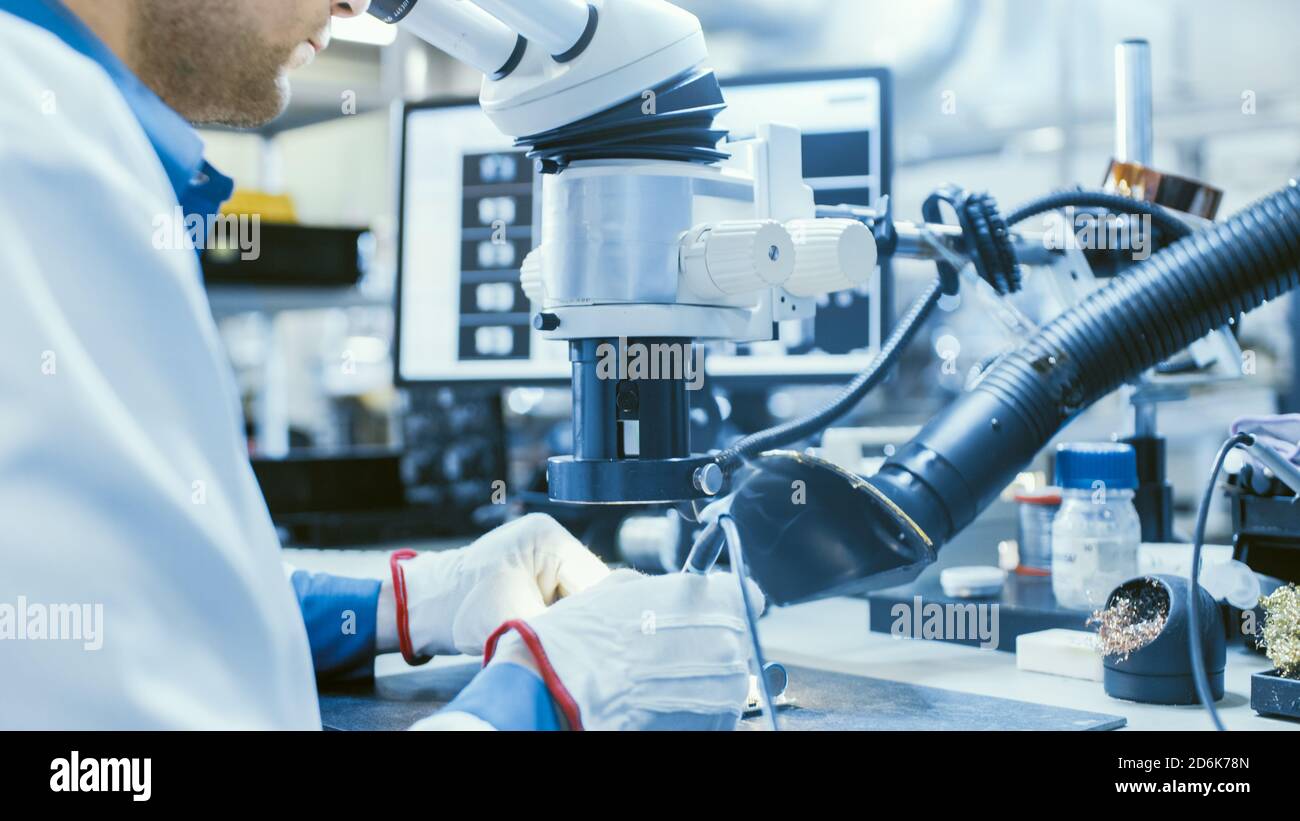 Nahaufnahme eines Arbeiters in der Elektronikfabrik in weißer Arbeitsschicht Löten einer Leiterplatte durch ein digitales Mikroskop. High-Tech-Fabrik Stockfoto