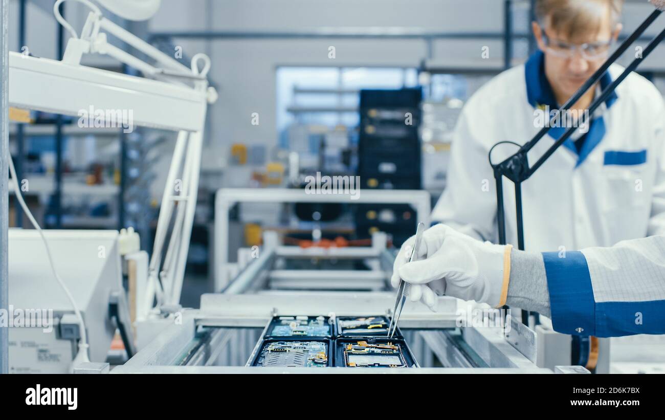 Aufnahme einer Elektronikfabrik Arbeiter Montage Leiterplatten von Hand, während es auf der Montagelinie steht. High-Tech-Fabrik. Stockfoto