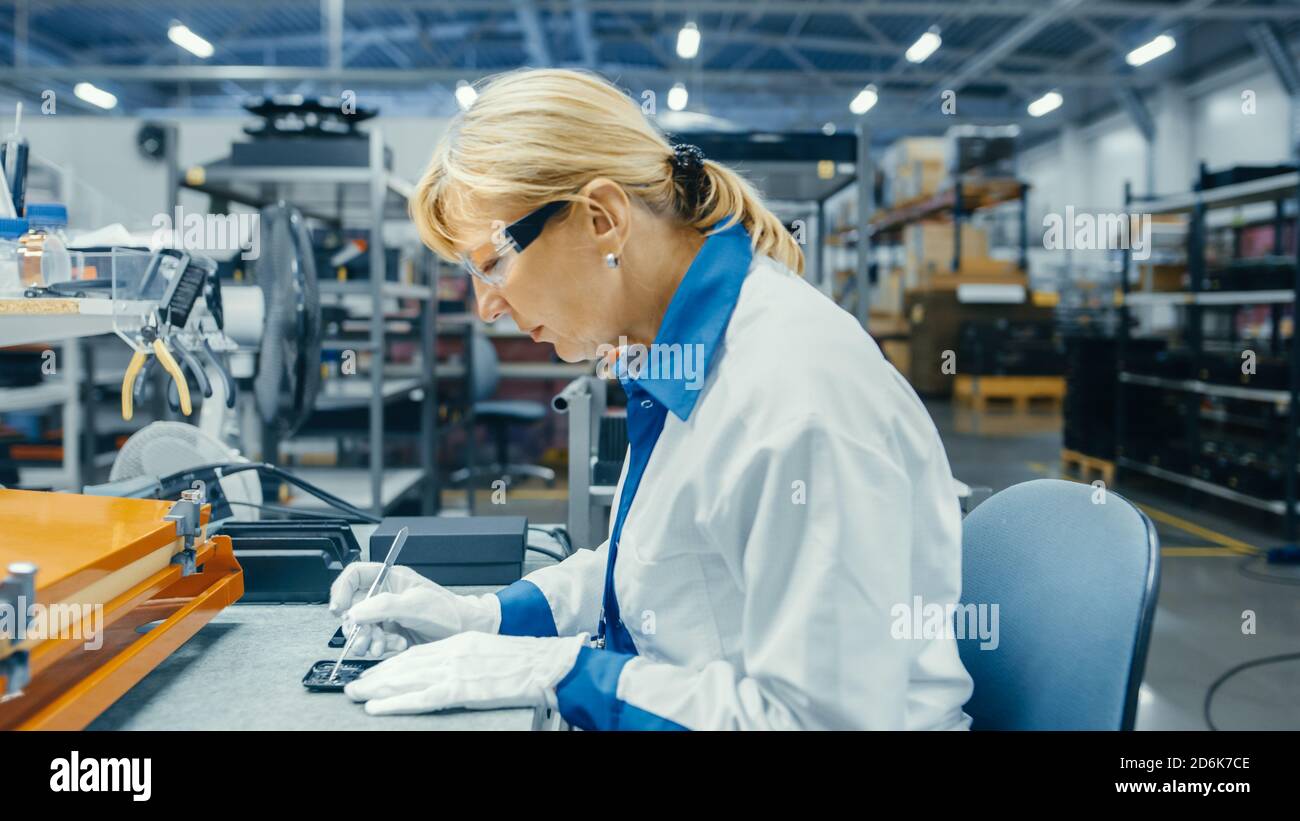 Leitender Arbeiter in der Elektronikfabrik in White Work Coats Mikrochips, Prozessoren und Halbleiter in Leiterplatten für Smartphones einsetzen Stockfoto