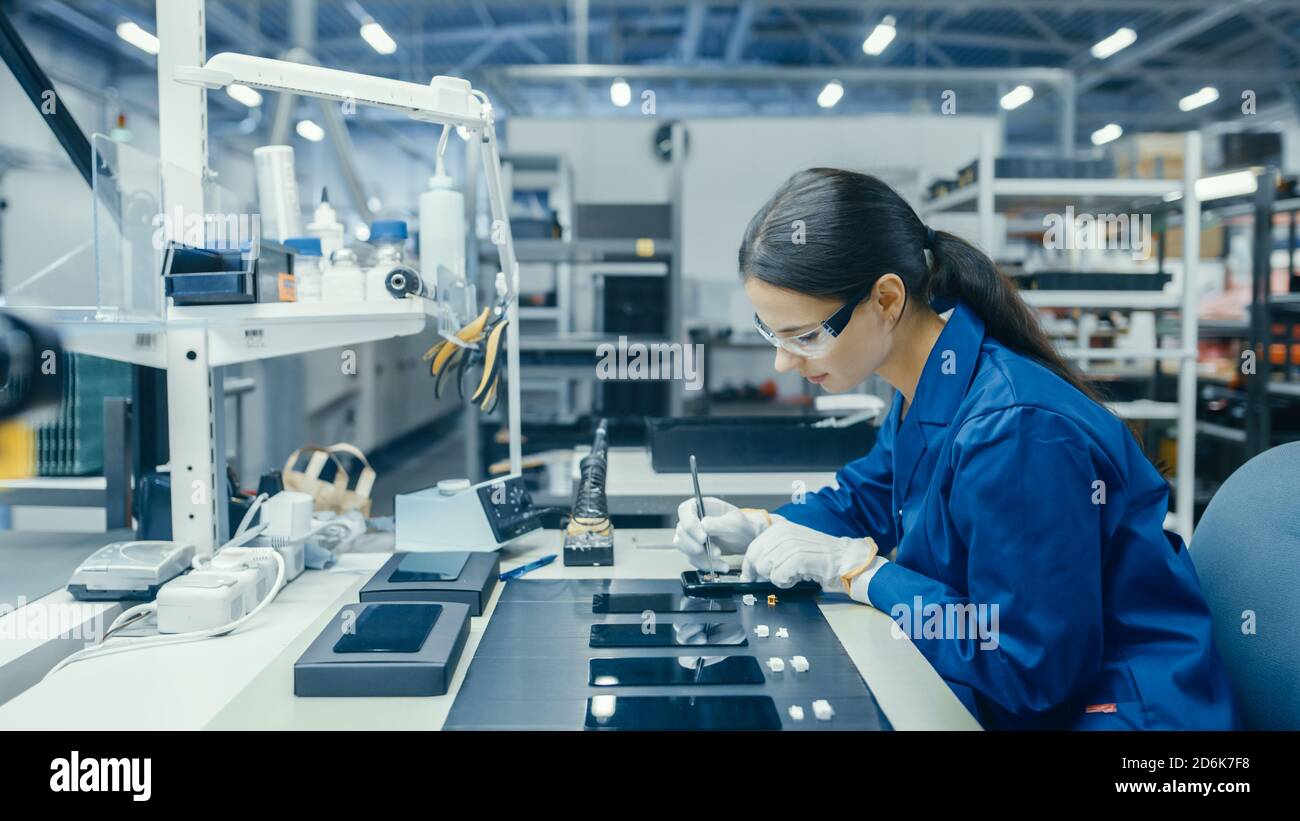 Young Female in Blue Work Coat ist die Montage von Leiterplatten für Smartphones. Arbeiter in der Elektronikfabrik in einer High-Tech-Fabrik. Stockfoto