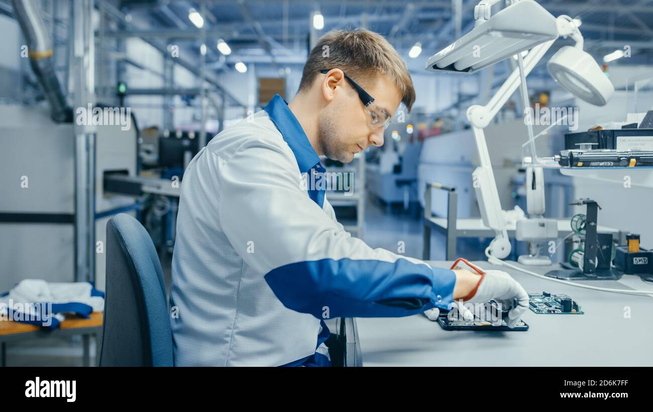 Junger Mann in Blau und Weiß Arbeitsmantel ist mit Zange zu gedruckten Leiterplatten für Smartphone montieren. Arbeiter in der Elektronikfabrik in einer High-Tech Stockfoto