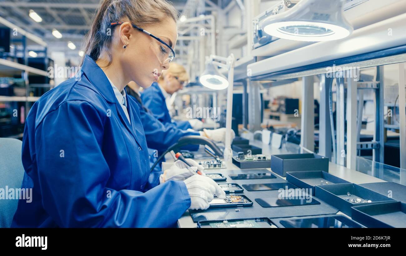 Woman Electronics Factory Worker in Blue Work Coat und Schutzbrille ist Montage Smartphones mit Schraubendreher. High-Tech-Fabrik mit Stockfoto