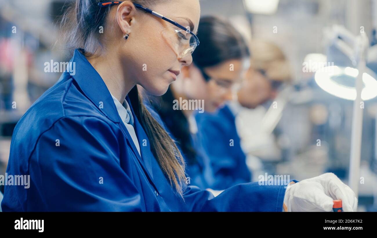 Weibliche Elektronik-Fabrik Arbeiter in blauer Arbeitsmantel und Schutzbrille ist Montage Laptop-Motherboard mit einem Schraubendreher. High-Tech-Fabrik Stockfoto