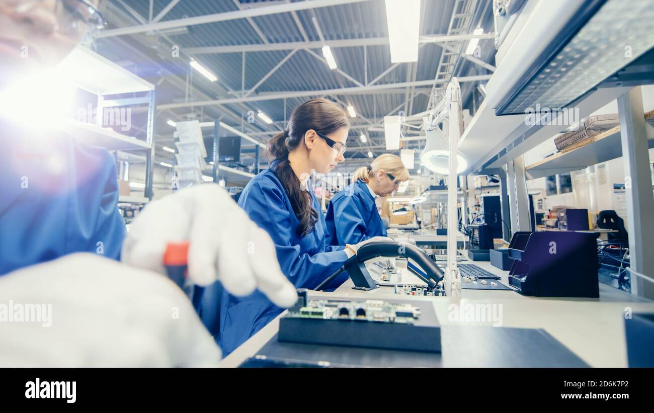 Weibliche Elektronik-Fabrik Arbeiter in blauer Arbeitsmantel und Schutzbrille ist Montage Laptop-Motherboard mit einem Schraubendreher. High-Tech-Fabrik Stockfoto