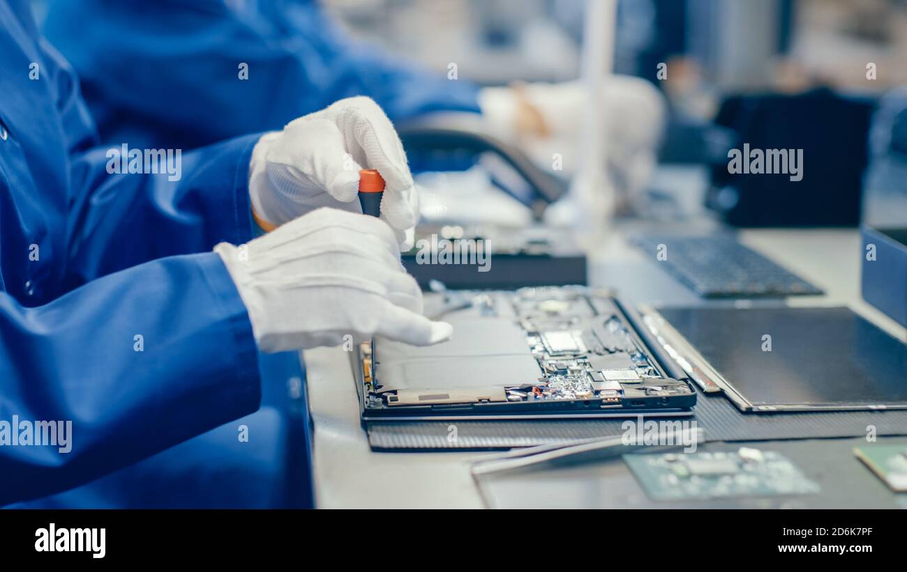 Nahaufnahme einer Arbeiterin in der Elektronikfabrik in blauem Arbeitsmantel Montage des Laptops auf dem Motherboard mit einem Schraubendreher. High-Tech-Fabrik mit Stockfoto