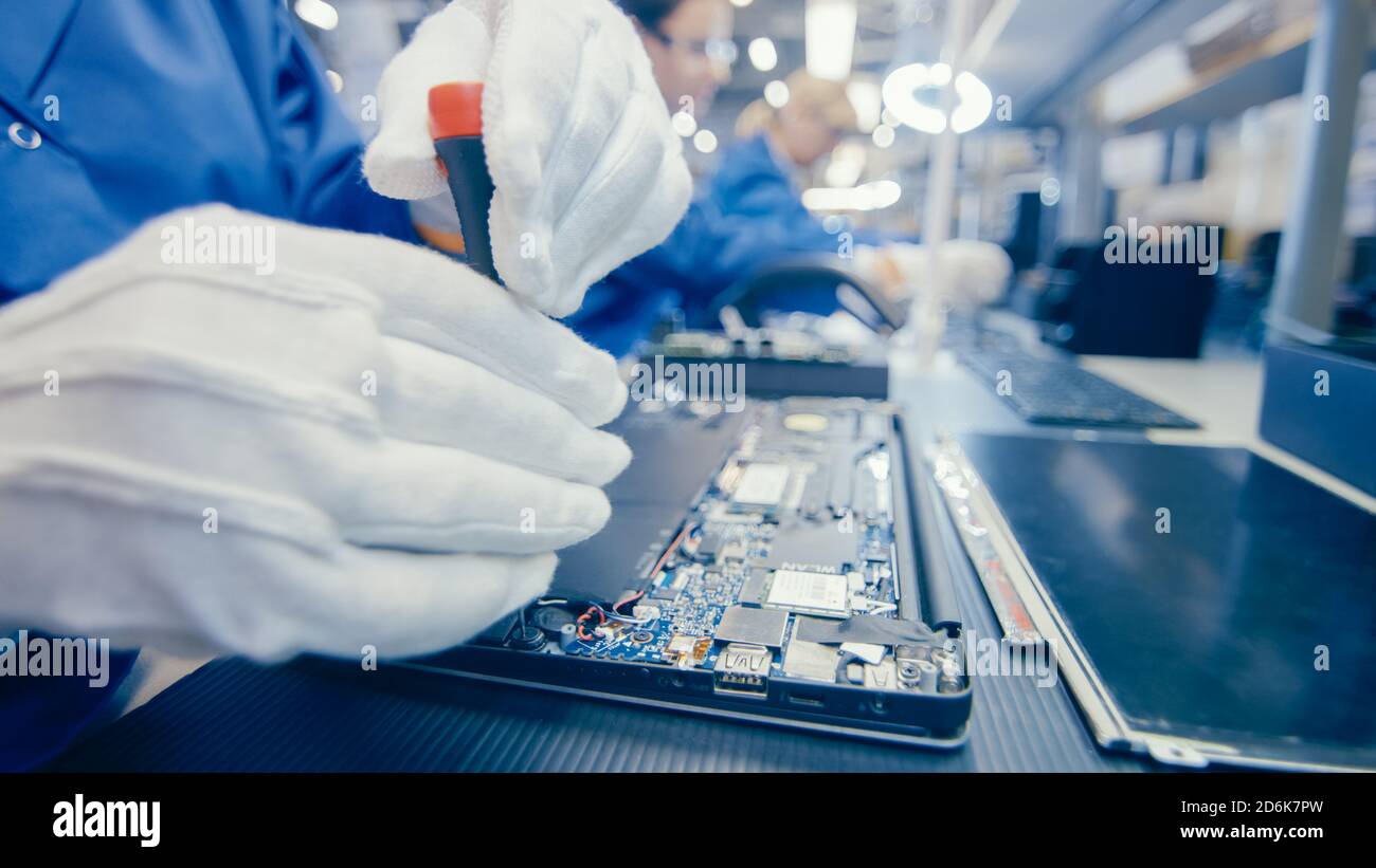 Nahaufnahme einer Arbeiterin in der Elektronikfabrik in blauem Arbeitsmantel Montage des Laptops auf dem Motherboard mit einem Schraubendreher. High-Tech-Fabrik mit Stockfoto