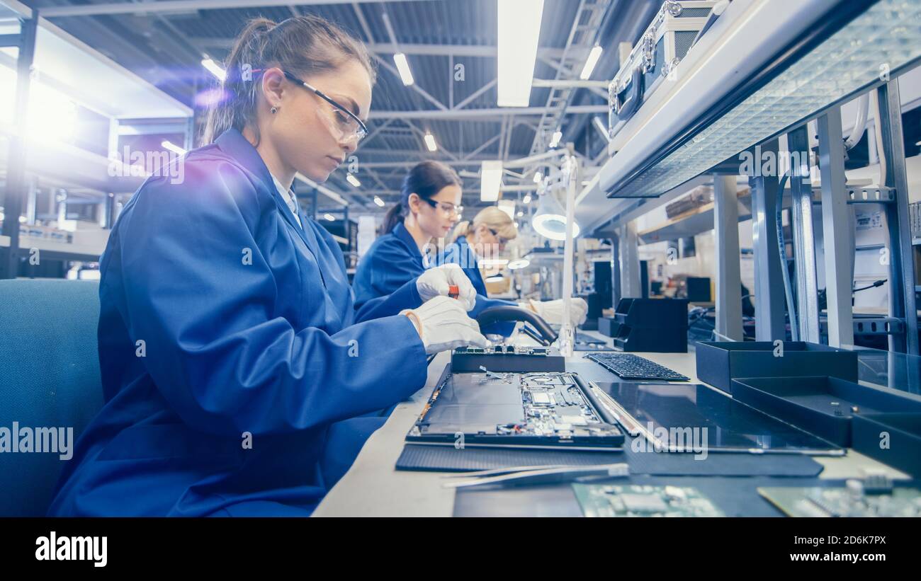 Woman Electronics Factory Worker in Blue Work Coat und Schutzbrille ist Montage Laptop Motherboard mit einem Schraubendreher. High-Tech-Fabrik Stockfoto