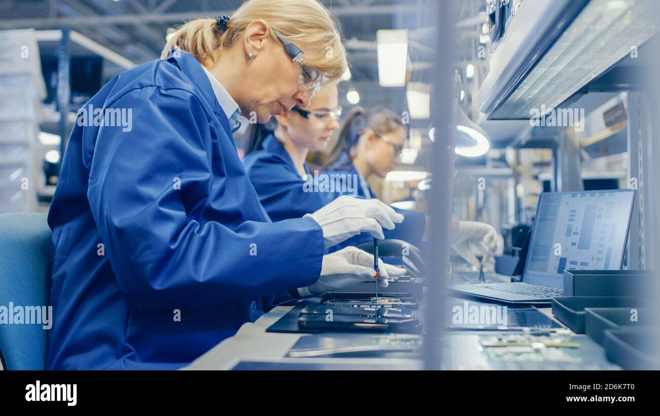 Weibliche Elektronik-Fabrik Arbeiter in Blue Work Coat und Schutzbrille ist Montage Smartphones mit Schraubendreher. High-Tech-Fabrik mit Stockfoto