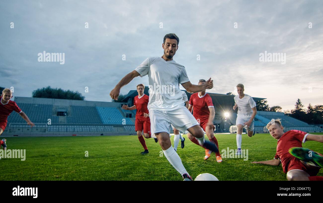 Der Profi-Fußballspieler geht den Mitgliedern des gegnerischen Teams aus und schießt den Ball, um das Tor zu schießen. Fußball-Meisterschaft auf einem Stadion. Stockfoto