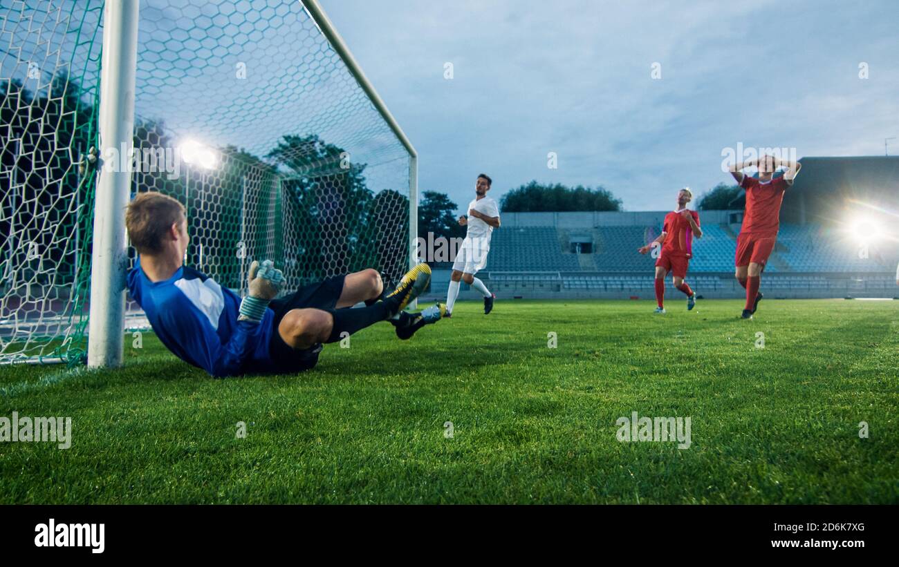 Auf Stadion-Angreifer tritt den Ball und erzielt das Tor, Fußball-Torwart versucht, Tore zu verteidigen, aber springt und scheitert an den Ball zu fangen. Stockfoto