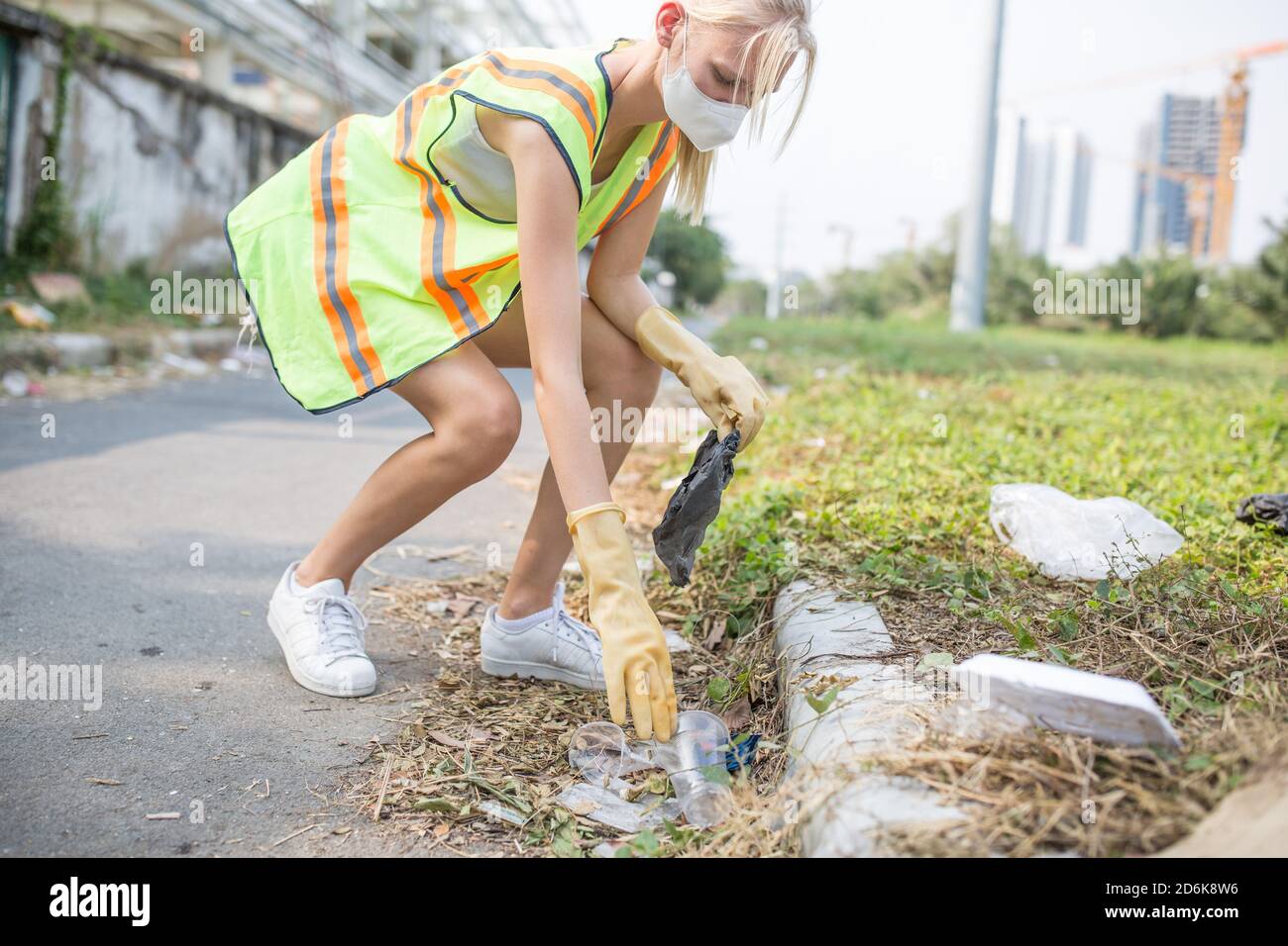 Weibliche Freiwillige Abholung Plastikmüll während einer Säuberung in der Stadt Umgebung trägt eine reflektierende Weste und Gesichtsmaske. Stockfoto