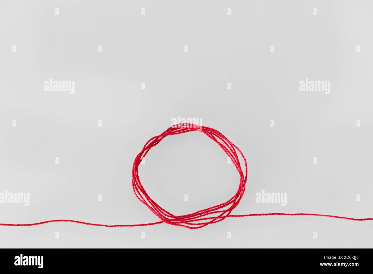 Ein roter Seidenfaden, kreisförmig geloopt, der sich an beiden Enden erstreckt und den roten Faden des Schicksals in der chinesischen Tradition symbolisiert, auf einem weichen weißen Hintergrund Stockfoto