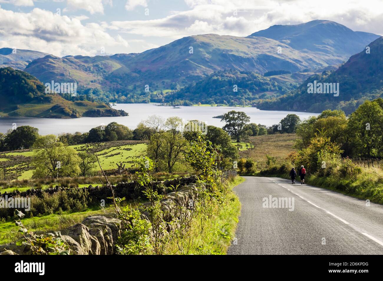 Steinmauer und Gras umragt an der A5091 Landstraße mit zwei Spaziergängern, die nach Ullswater im Lake District National Park laufen. Dockray Cumbria England Großbritannien Stockfoto