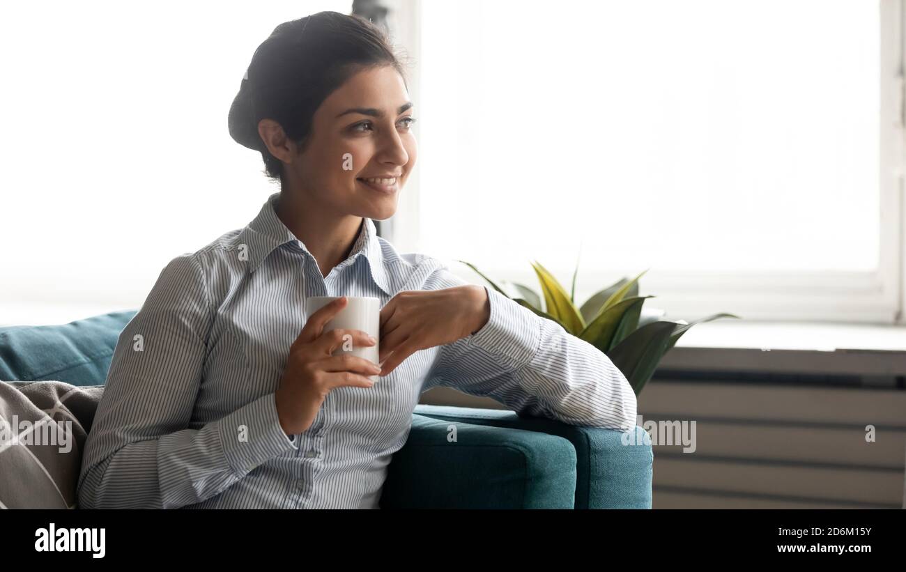 Indische Frau träumt mit einer Tasse Tee, während sie sich drinnen ausruhen Stockfoto