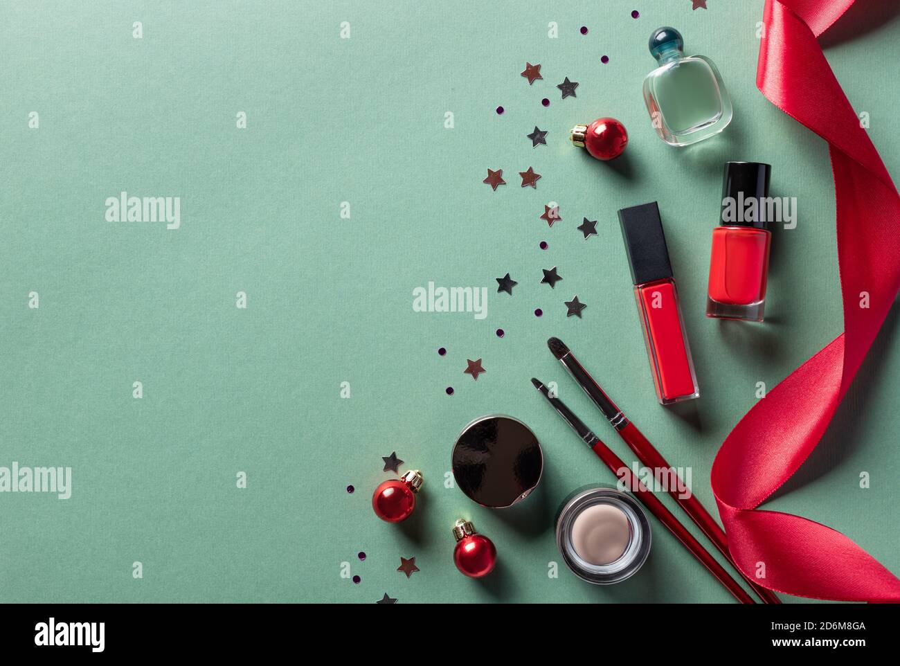 Kosmetische Make-up-Produkte auf grünem Hintergrund mit Weihnachtsdekor. Stockfoto