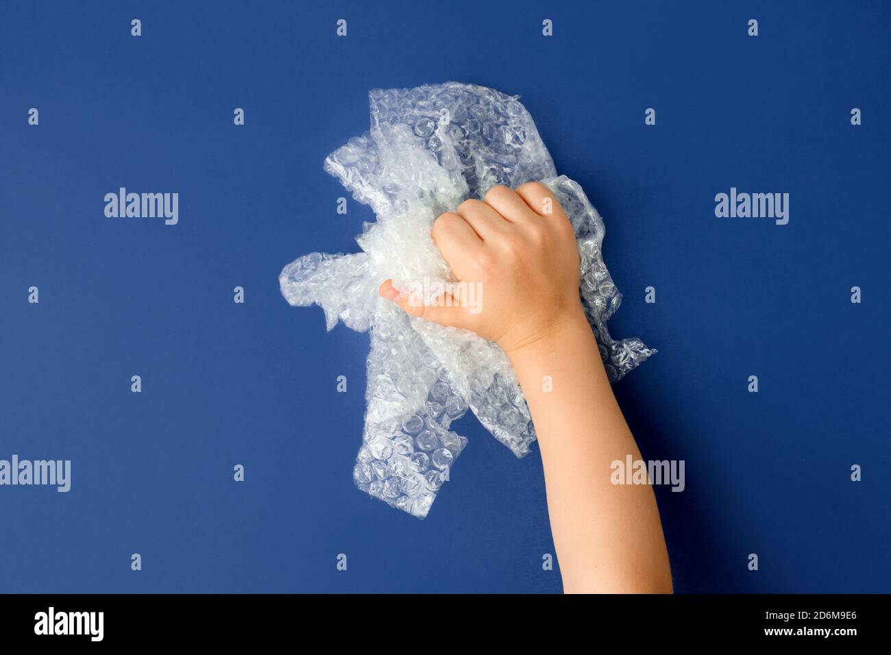 Hand knallen eine Blase wickeln auf klassischen blauen Hintergrund, Anti-Stress-Therapie-Konzept, seltsam befriedigend semi surreal asmr Stockfoto