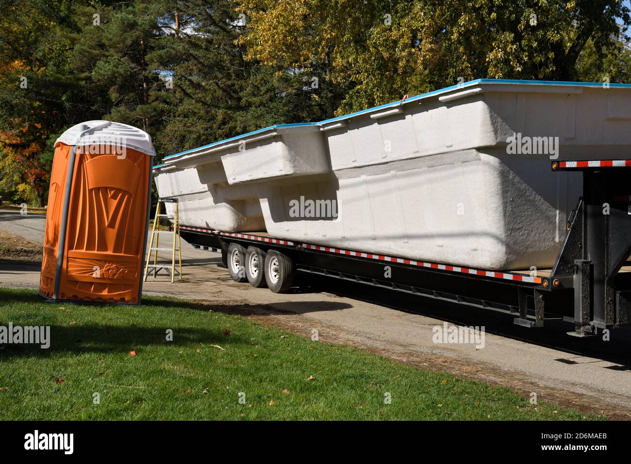 Fiberglas Pool Shell auf Pritschenwagen Anhänger auf der Straße mit Orange tragbare Toilette in Barrie Kanada im Herbst Stockfoto
