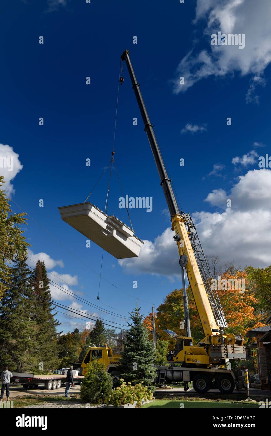 Hoher Kran heben Fiberglas Schwimmbad Schale über Hydro Power Linien und Haus zu Hinterhof im Herbst Stockfoto