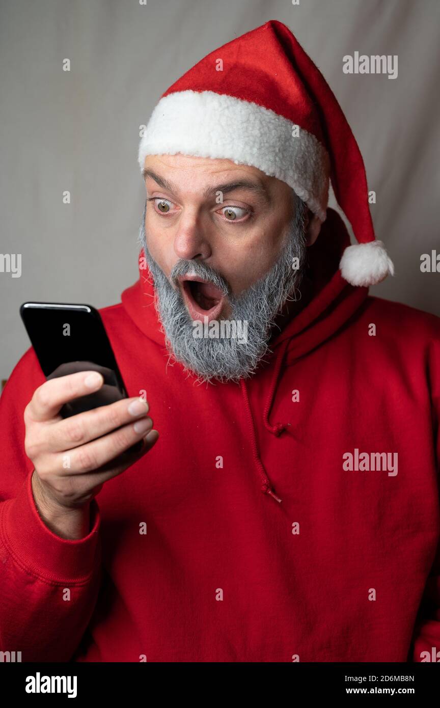 Der Weihnachtsmann schaut mit seinem Mund auf ein Handy Weit offen Stockfoto