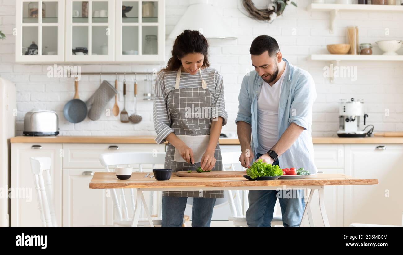 Glückliches junges Paar, das gemeinsam Salat in der modernen Küche zubereitet Stockfoto