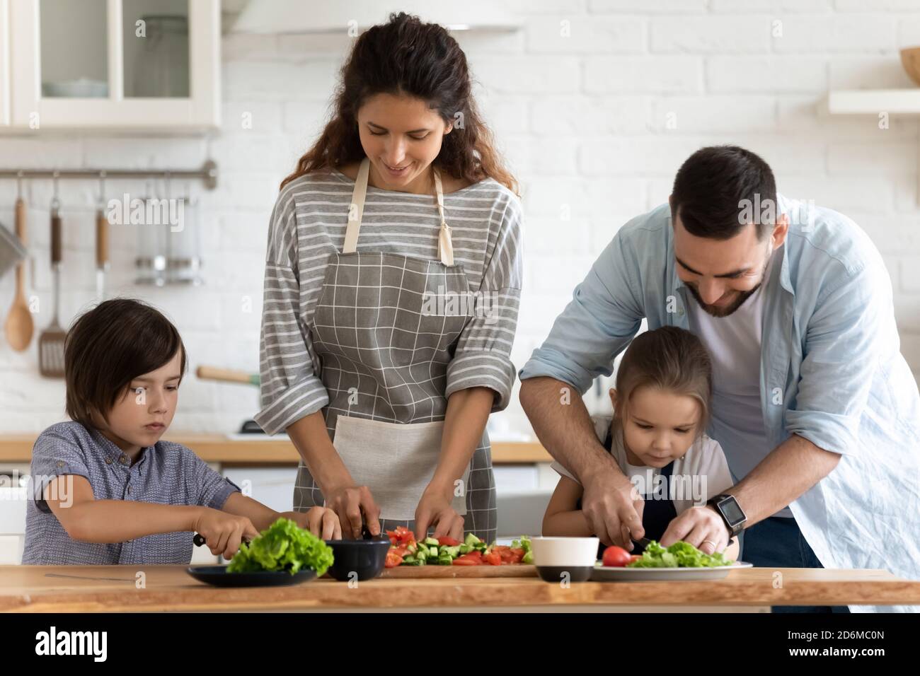 Glückliche Familie mit zwei kleinen Kindern, die Salat kochen, Gemüse schneiden Stockfoto