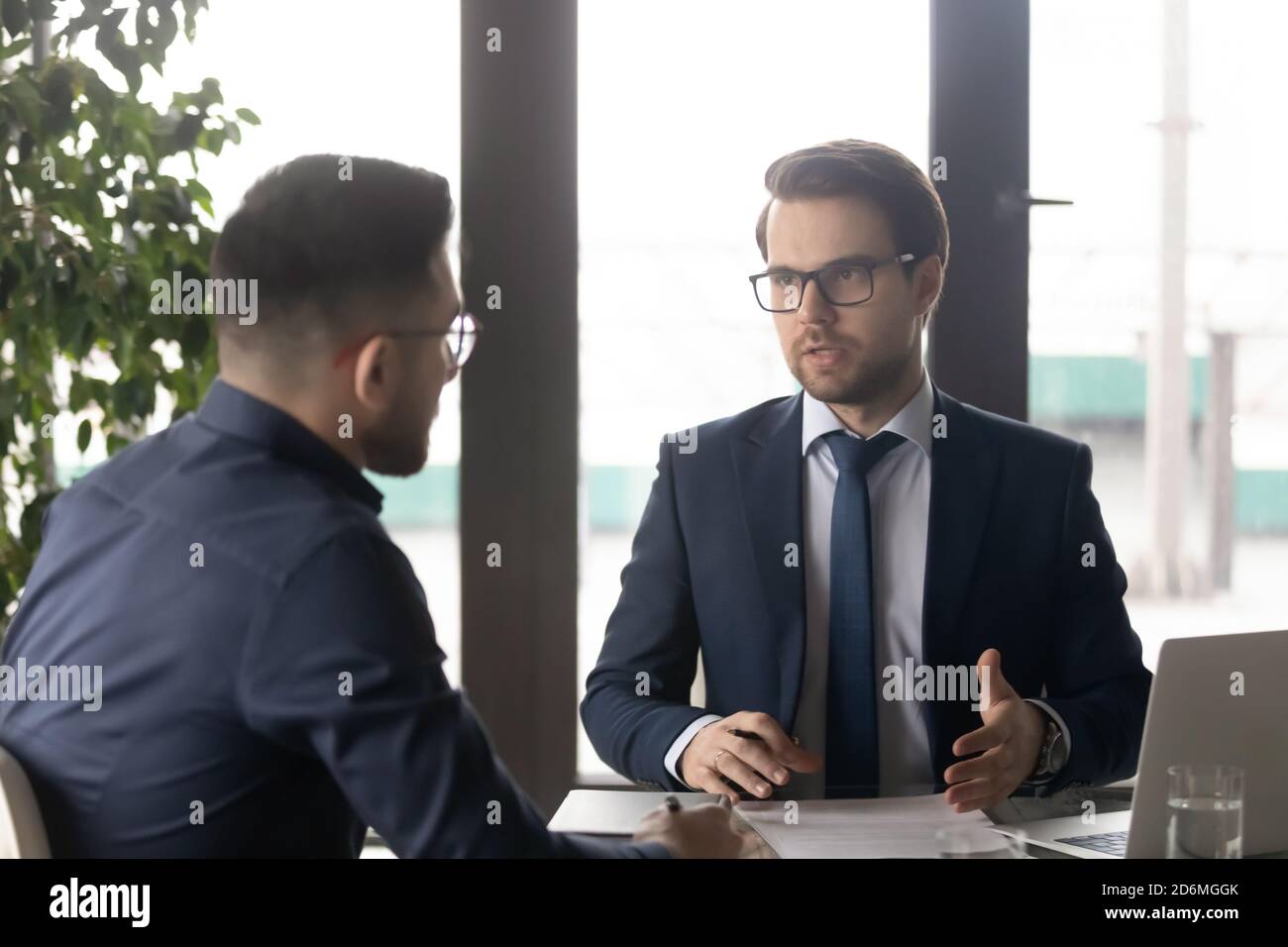 Fokussierter junger Geschäftsmann in formeller Kleidung im Gespräch mit Partner. Stockfoto