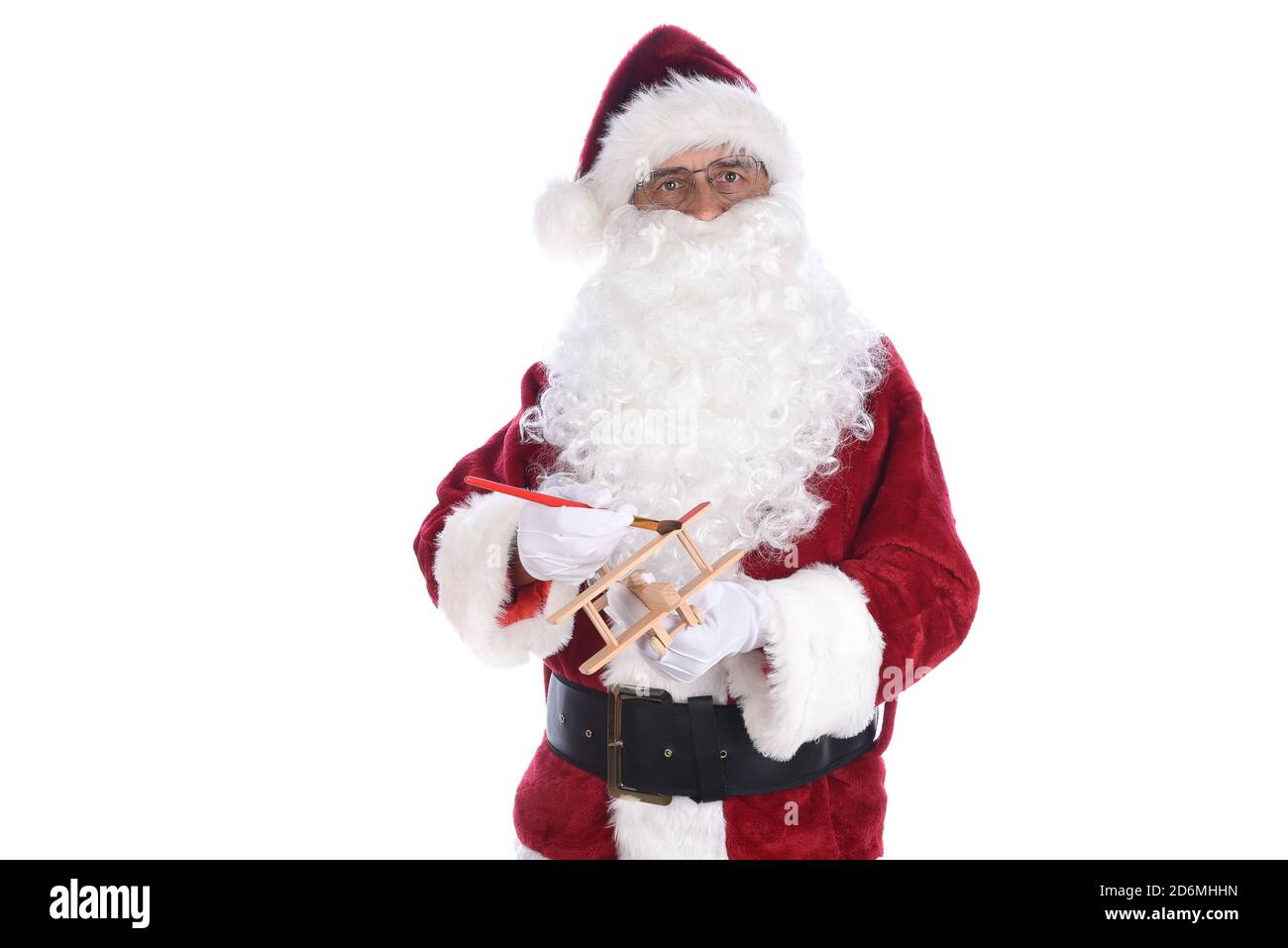 Älterer Mann trägt ein traditionelles Weihnachtsmann-Kostüm und malt ein Spielzeug aus Holz. Isoliert auf Weiß. Stockfoto