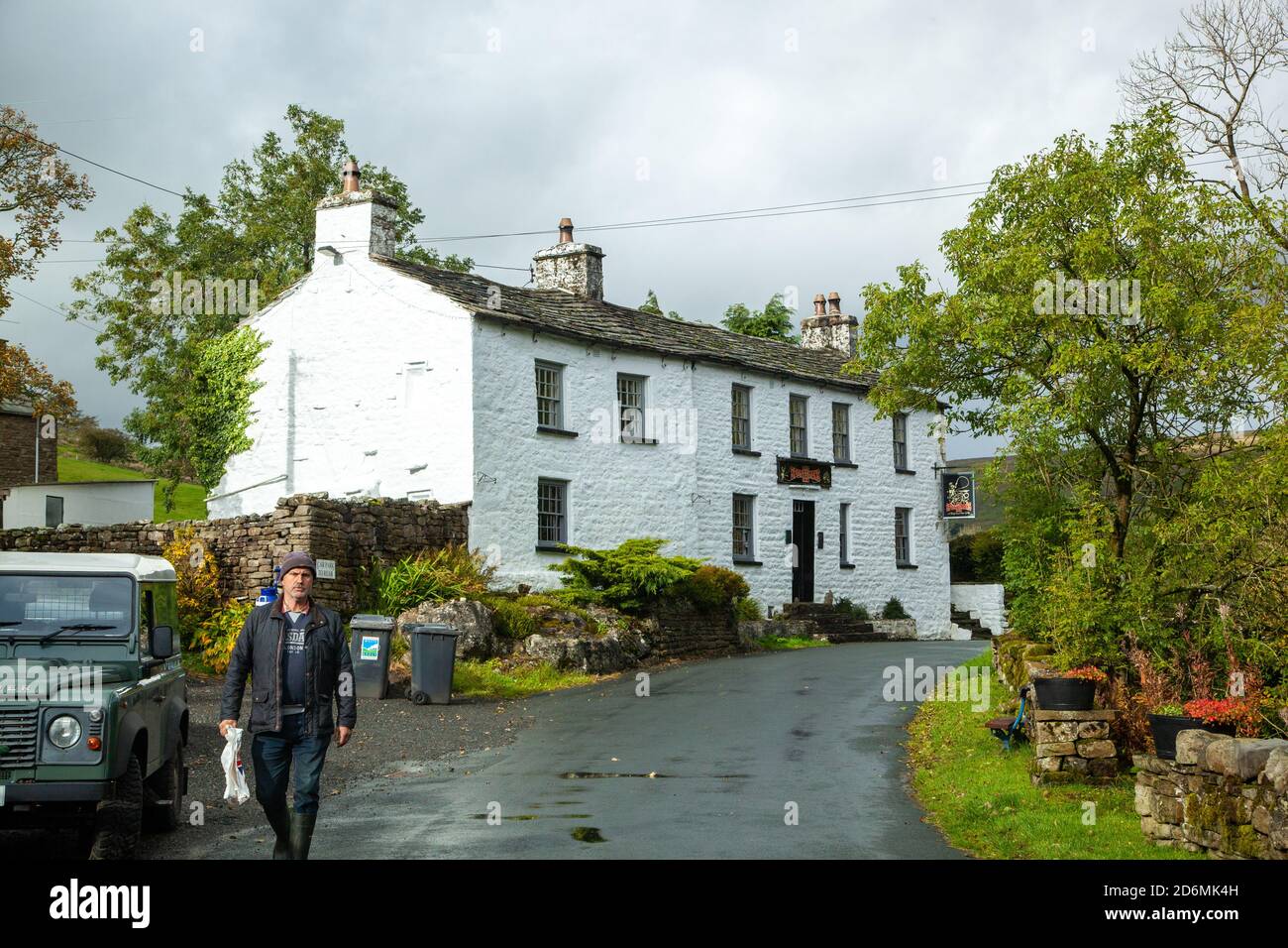 Mann, der am Sportmans Inn und einem Landrover Defender vorbeigeht In Cowgill Sedbergh North Yorkshire England Stockfoto
