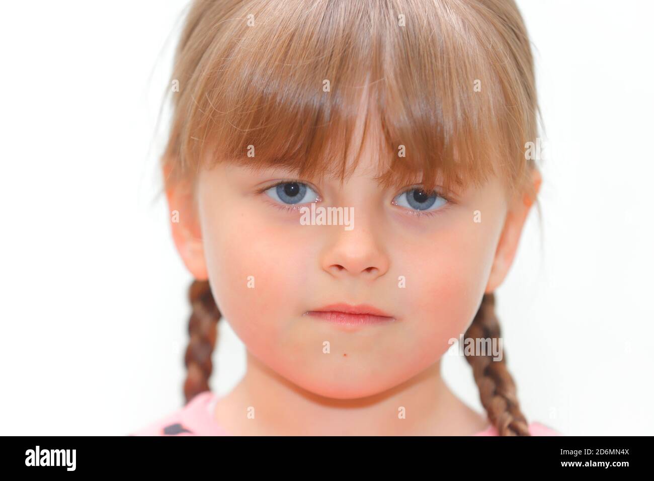 Ein 5-jähriges Mädchen mit Zöpfen und einem leeren Gesichtsausdruck vor weißem Hintergrund. Stockfoto