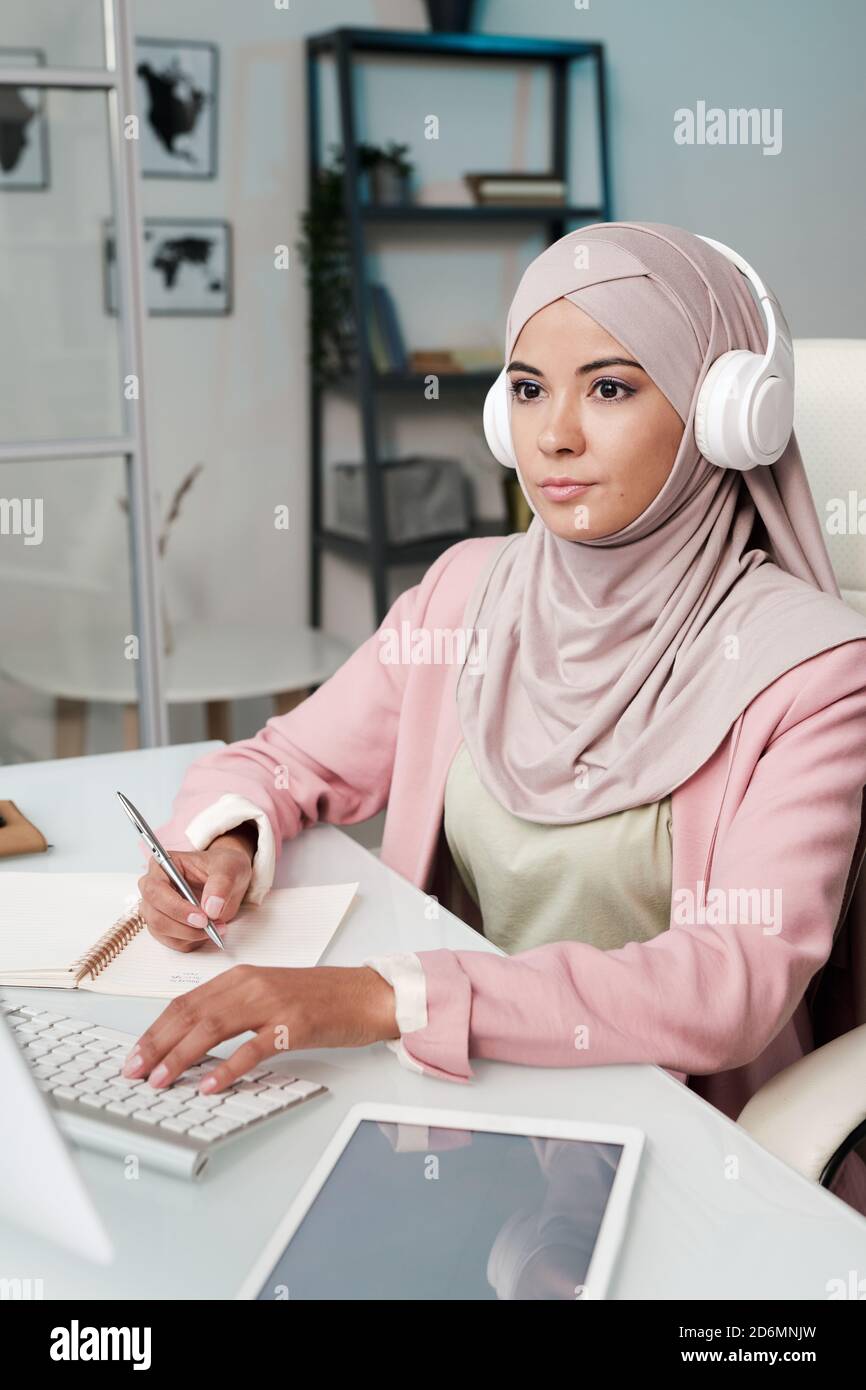 Junge ernsthafte muslimische Frau in Kopfhörer, Hijab und intelligente Casualwear Stockfoto