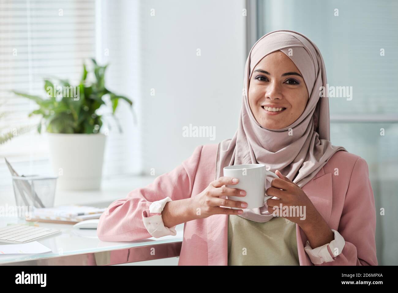Junge erfolgreiche muslimische Geschäftsfrau in Hijab mit Tee oder Kaffee In der Pause Stockfoto