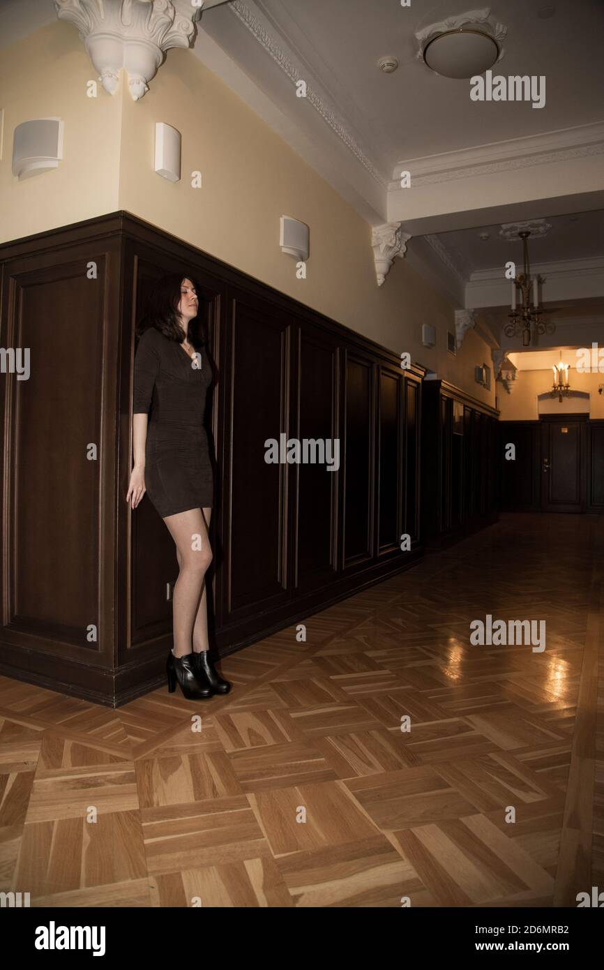 Mädchen in kurzen Kleid steht in einem Korridor mit dem Rücken gegen eine Holzwand; sie scheint erschrocken; die Atmosphäre ist geheimnisvoll und/oder beängstigend; Konzept Stockfoto