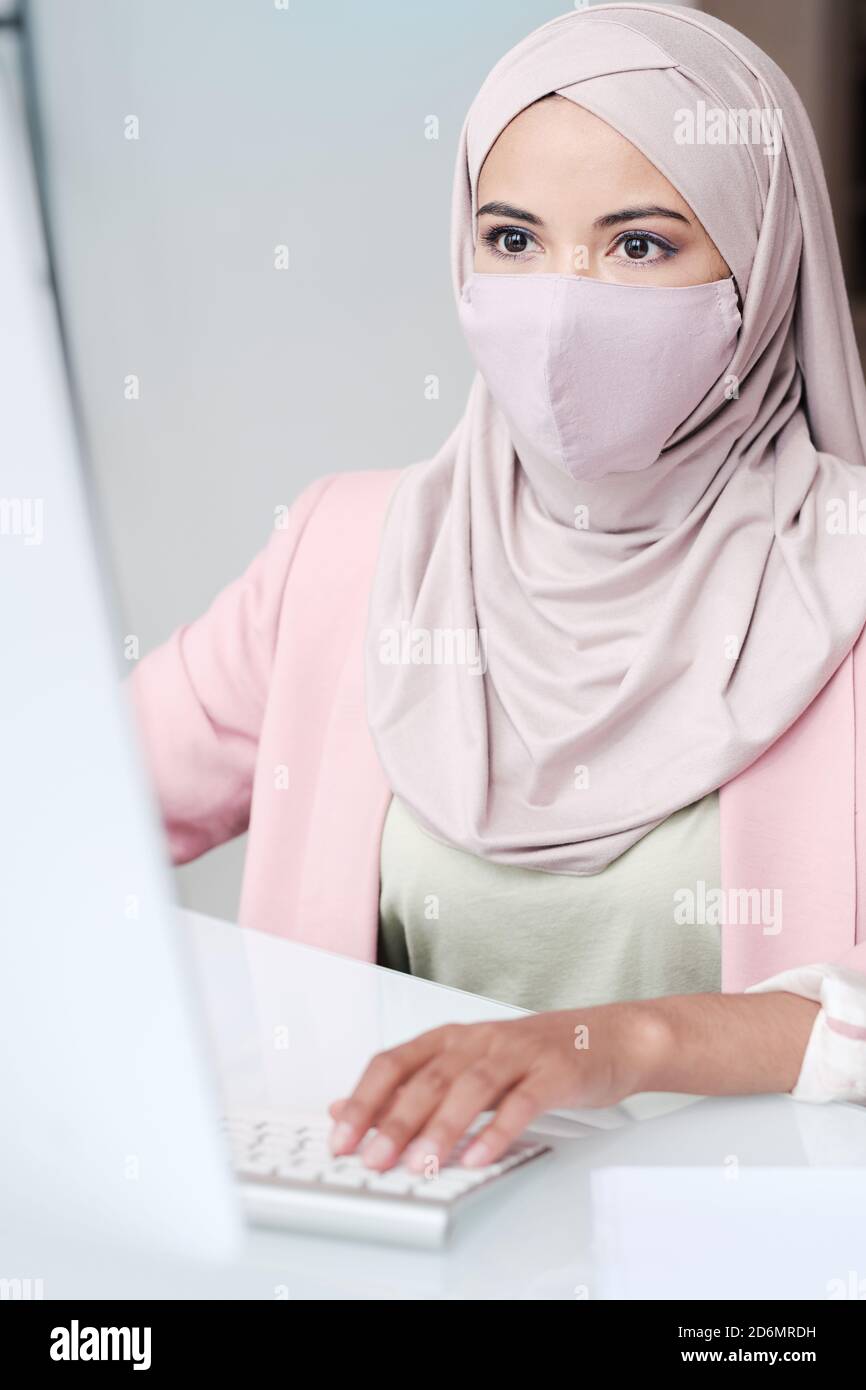 Junge zeitgenössische Geschäftsfrau in Hijab und Schutzmaske Analyse von Daten Stockfoto