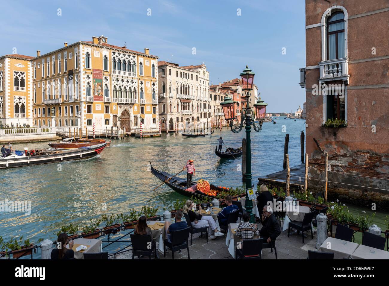 Touristen genießen die Aussicht von einem Restaurant am Kanal auf Palazzo Cavalli-Franchetti und Palazzo Barbaro. Gondelbahn (Gondoliere) auf dem Canal Grande, Venedig, Stockfoto