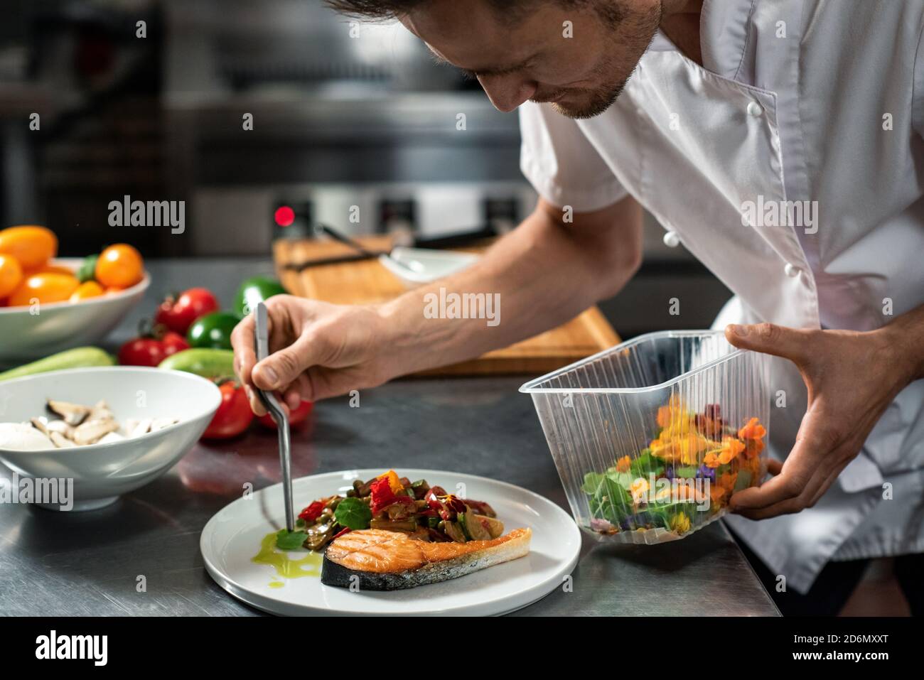 Junger männlicher Koch verzierend gebratenes Gemüse auf Stück gebraten Lachs auf dem Teller Stockfoto