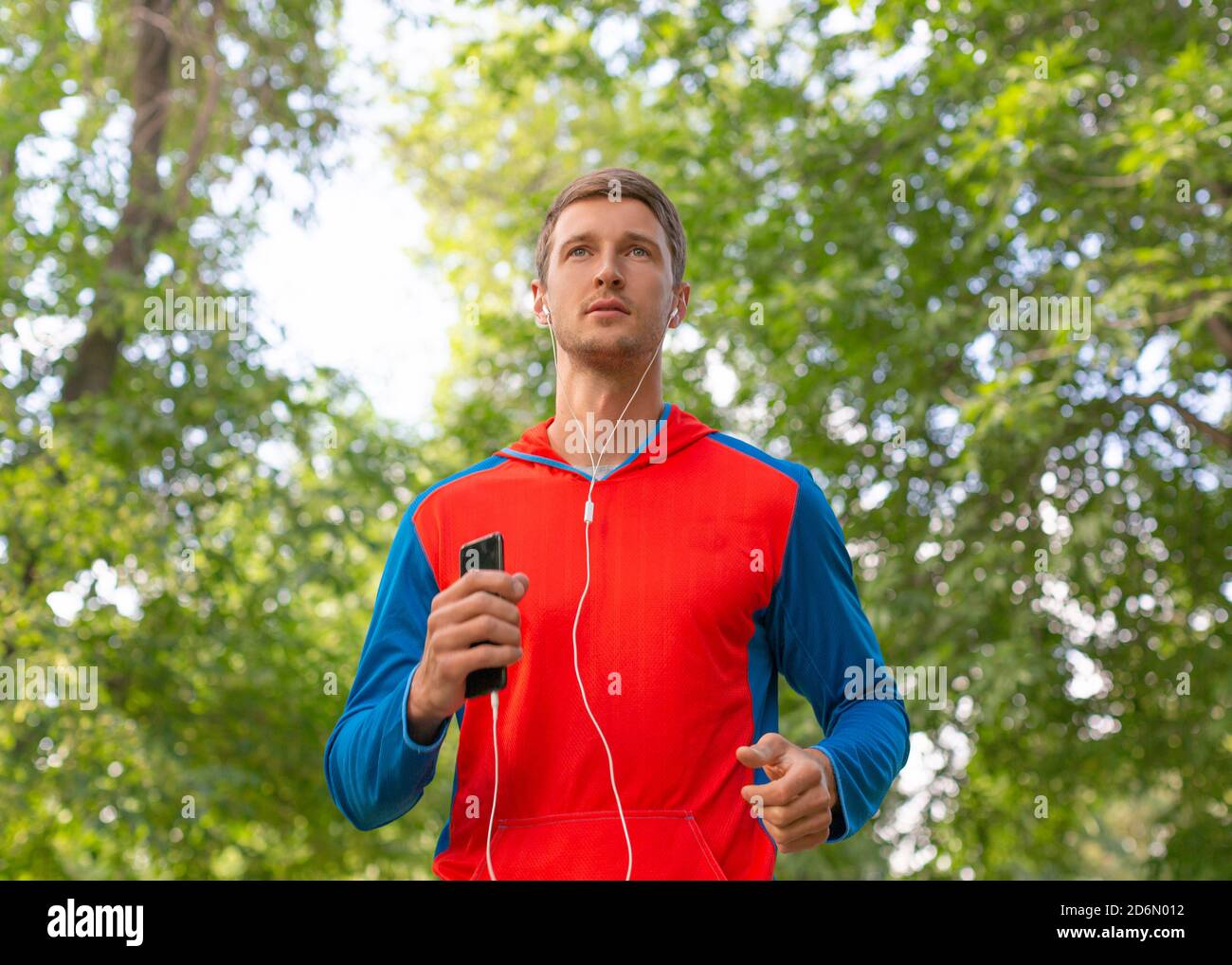 Sportler läuft entlang der Straße im Wald. Er hört die Musik über Kopfhörer. Das Konzept von Sport und einem gesunden Lebensstil. Stockfoto