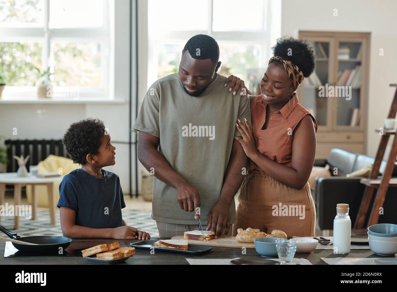 Junger afrikanischer Mann, der Sandwiches zum Frühstück zwischen seiner Frau zubereitet Und Sohn Stockfoto