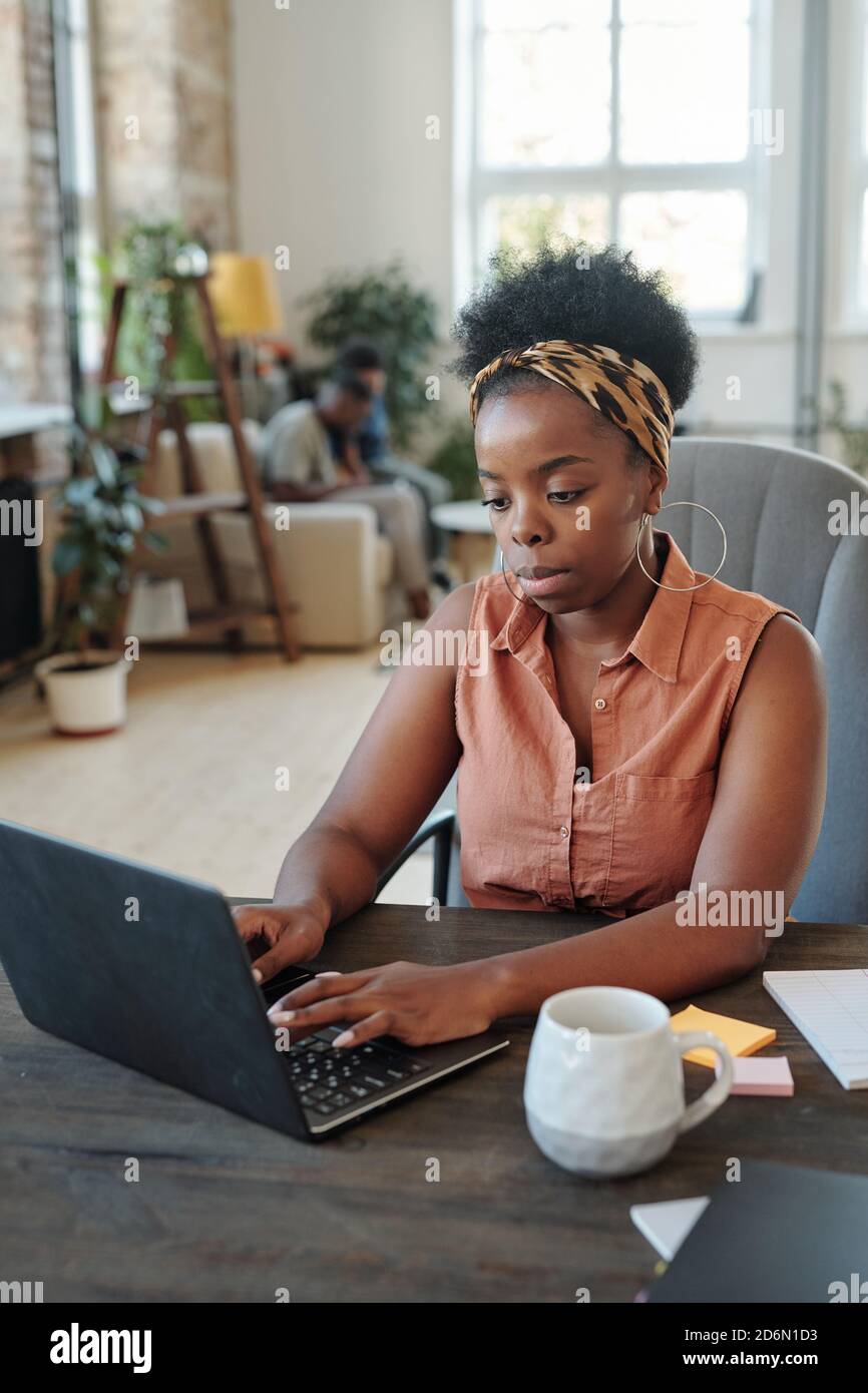 Seriöse junge afrikanische Freiberuflerin Networking vor dem Laptop Zu Hause Stockfoto