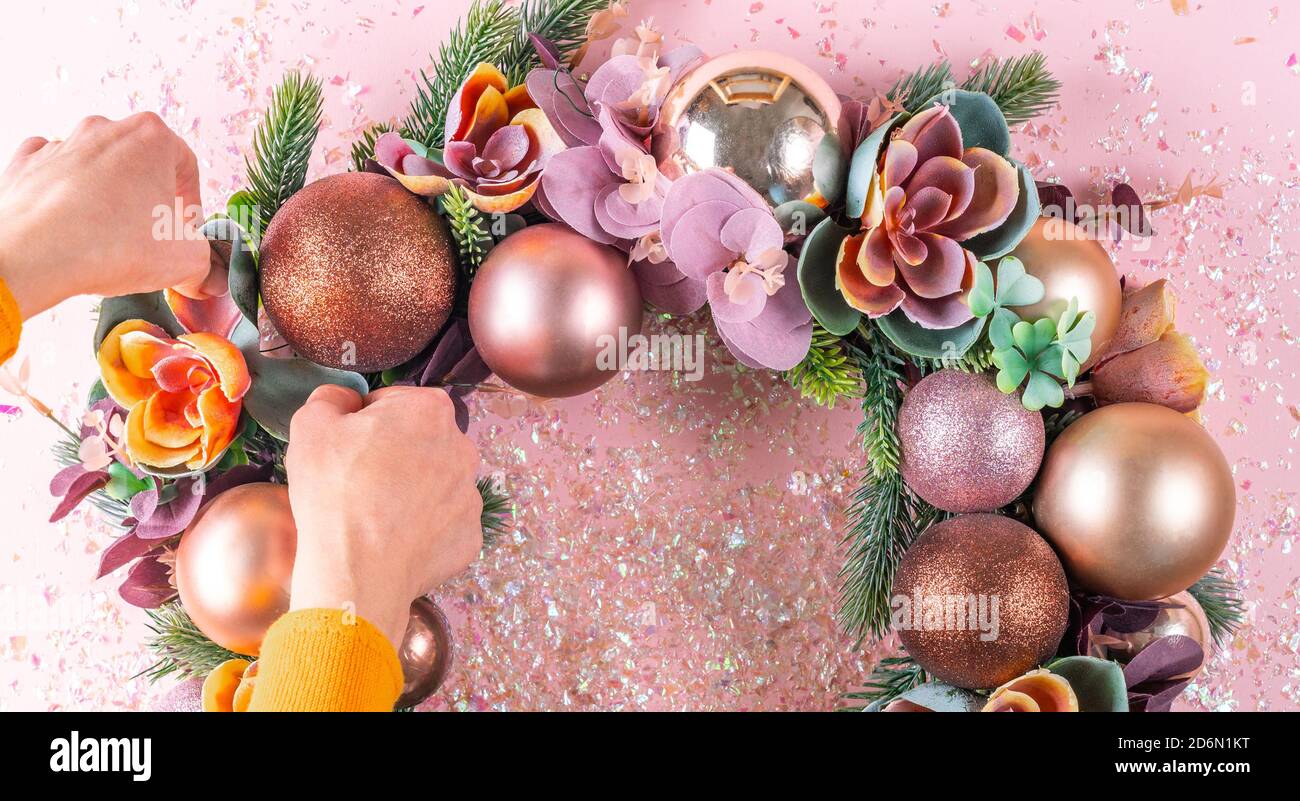 Weibliche Hand Dekoration schöne ungewöhnliche Weihnachtskranz auf rosa Hintergrund. Flach legen Stockfoto