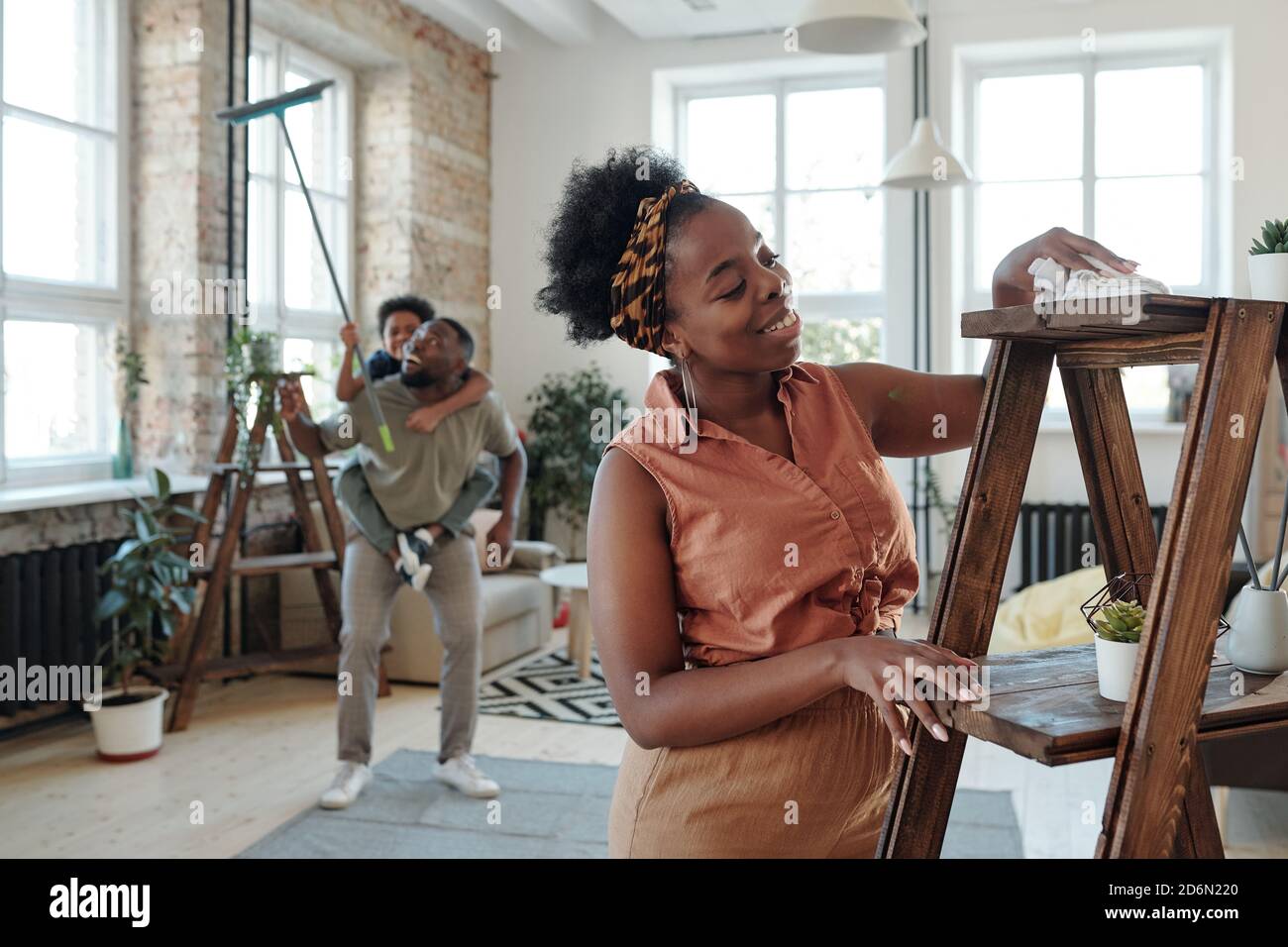 Glücklich junge Hausfrau der afrikanischen Ethnizität Reinigung Holzregale mit duster Stockfoto