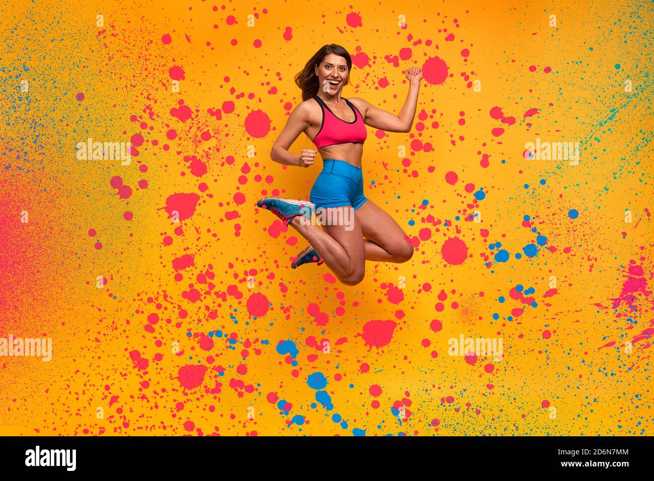 Sport Frau springt auf einem gelben Hintergrund. Fröhlicher und freudiger Ausdruck. Sprüheffekt Stockfoto