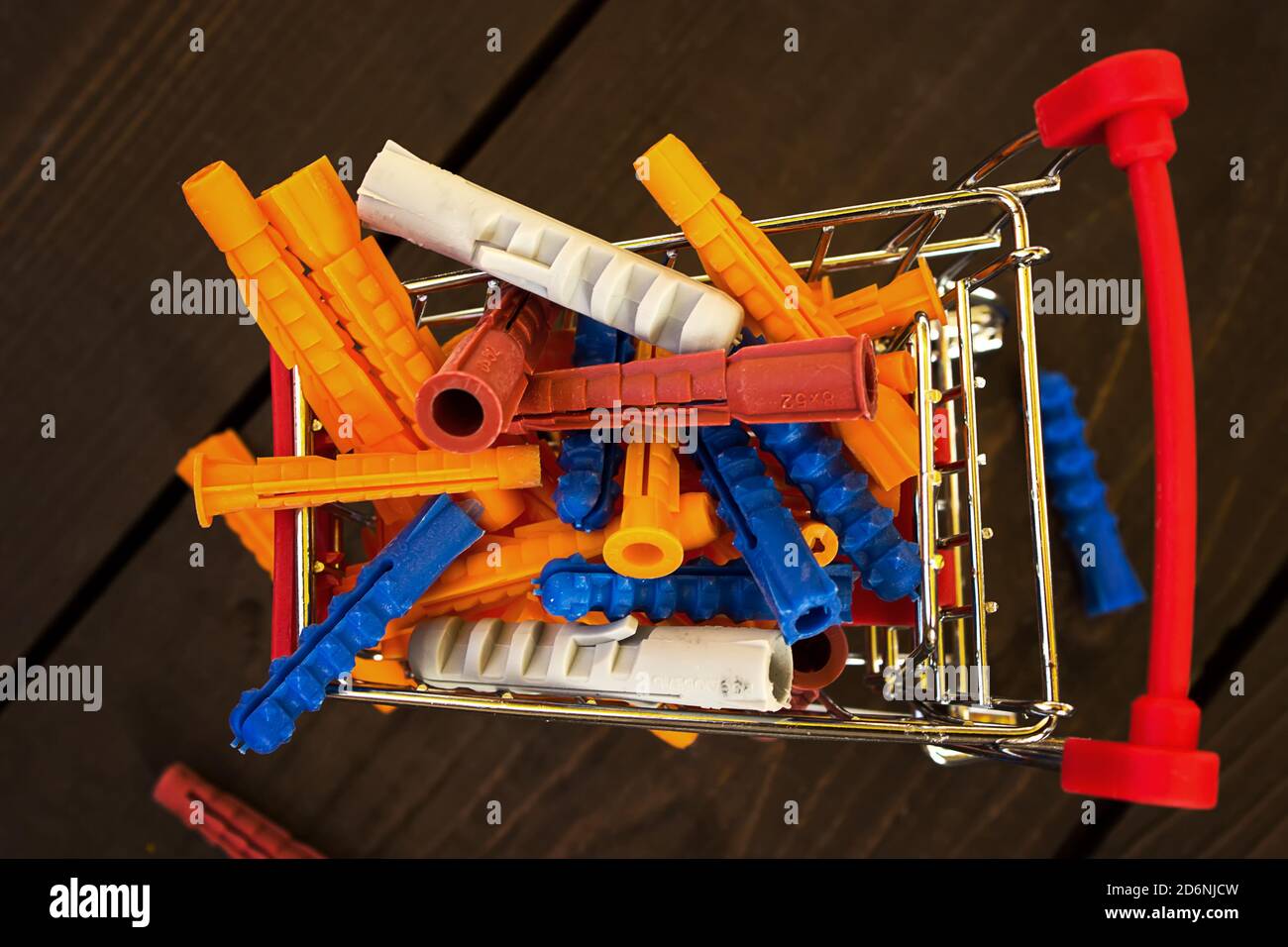 Stapel von bunten Kunststoff Dübel in Miniatur-Warenkorb. Shopping für Hausreparaturen Konzept. Draufsicht. Nahaufnahme Stockfoto