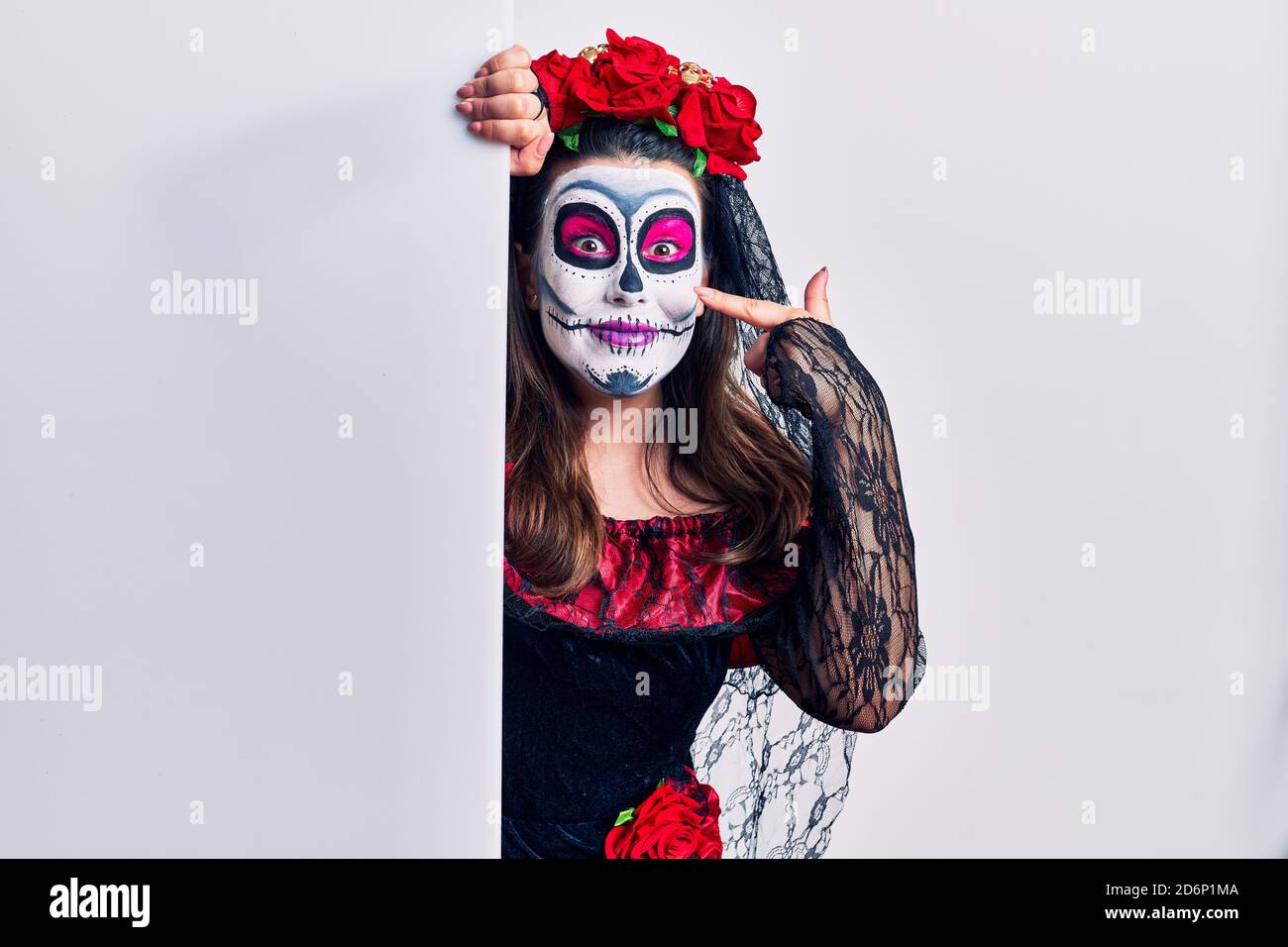Junge Frau trägt Tag der Toten custome hält leere leere Banner mit der Hand Finger auf Gesicht und Nase, lächelnd fröhlich. Beauty-Konzept Stockfoto