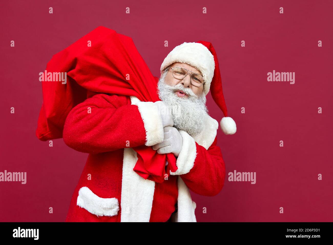 Müde Weihnachtsmann Gefühl Rückenschmerzen hält schwere Tasche auf rotem Hintergrund. Stockfoto